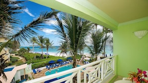 A balcony with a view of a pool and beach, surrounded by palm trees and blue umbrellas. - Dover Beach Hotel (St. Lawrence Gap)