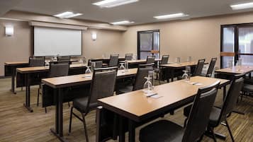 Un salón de conferencias con varias mesas y sillas, una pantalla de proyector y un amplio ventanal.