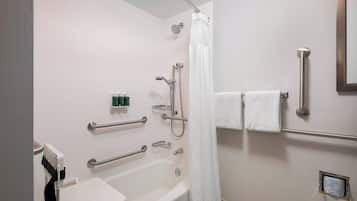 A bathroom with a bathtub, shower, and handrails.
