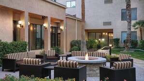 An outdoor patio area with wicker furniture, a central fire pit, and a well-maintained garden with various plants and flowers. - Courtyard by Marriott Las Vegas Convention Center (Las Vegas)