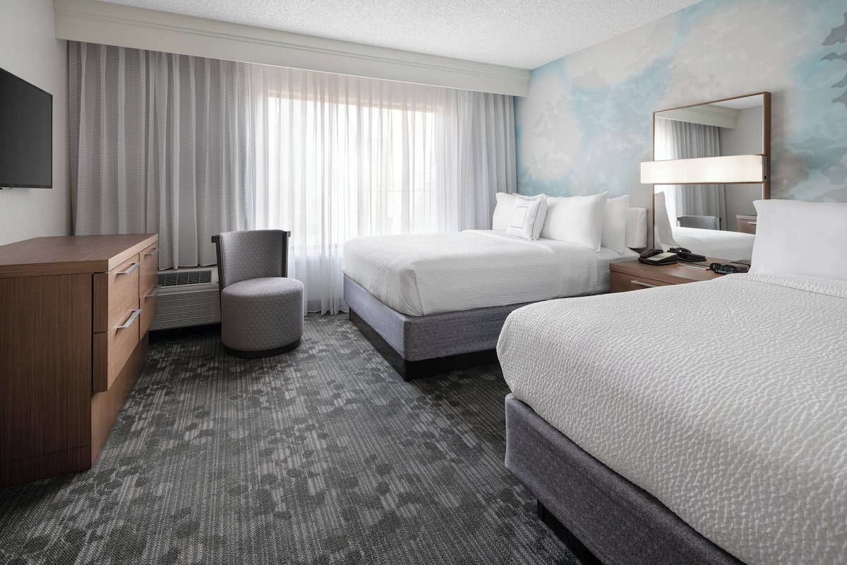 Quarto de hotel com uma cama grande, uma escrivaninha, uma cadeira e uma televisão.