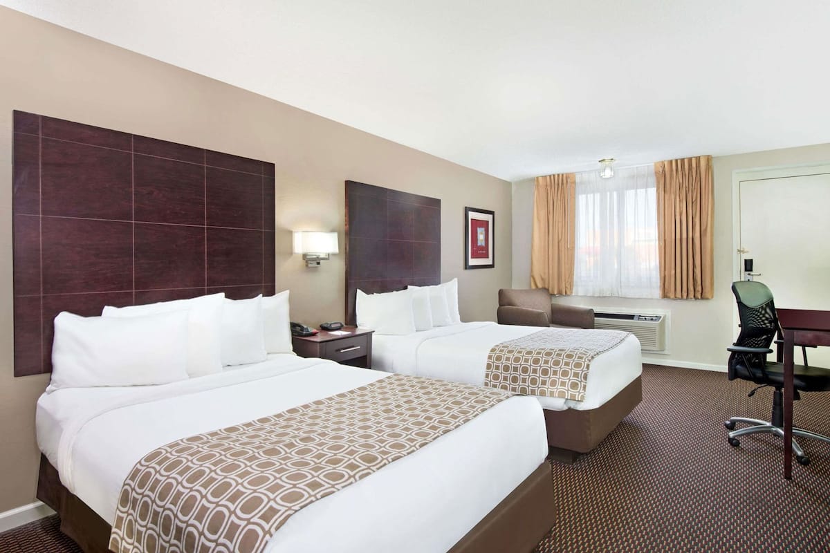 A hotel room with two beds, a desk, a chair, a lamp, and a window with curtains.