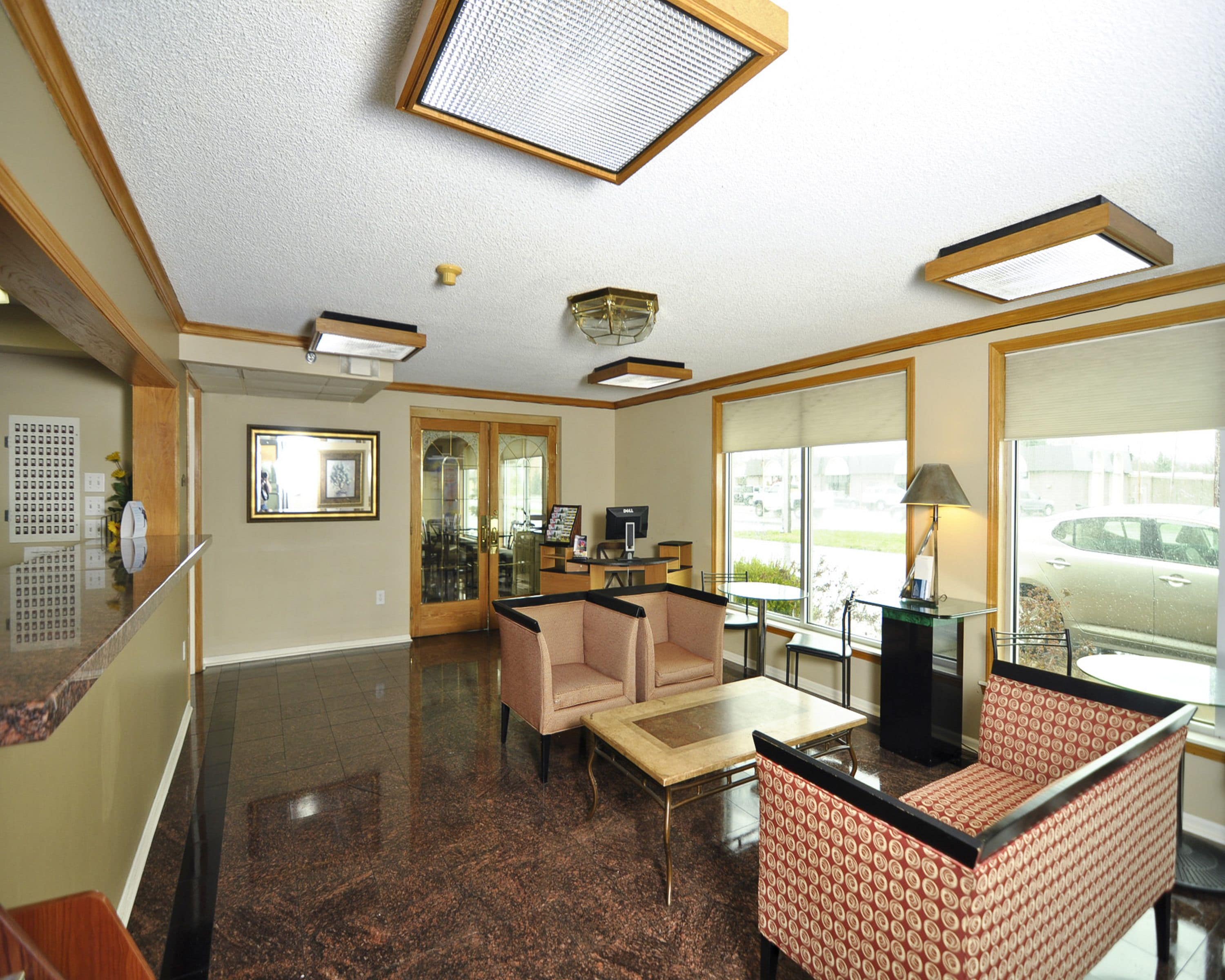 A hotel lobby with a reception desk, seating area, and large windows offering a view of the parking lot.