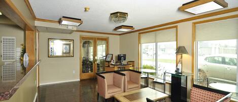 A hotel lobby with a reception desk, seating area, and large windows offering a view of the parking lot.