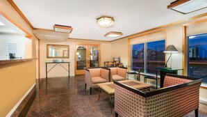 Un vestíbulo de hotel con mostrador de recepción, zona de estar con sofás y sillones, una pequeña mesa y grandes ventanales con vistas al exterior.
