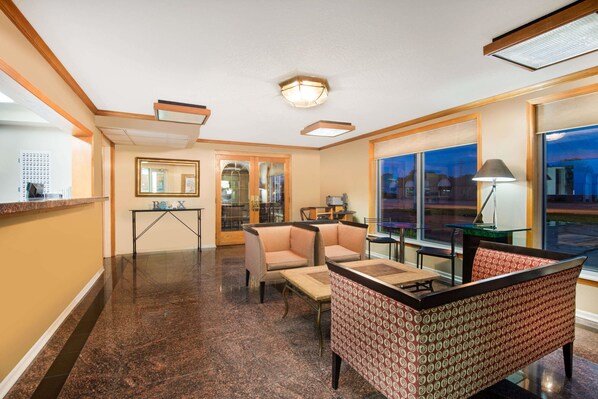 A hotel lobby with a reception desk, seating area with sofas and chairs, a small table, and large windows offering a view of the outside.