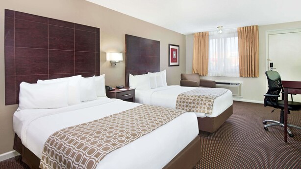 Una habitación de hotel con dos camas, un escritorio, una silla, una lámpara y una ventana con cortinas.