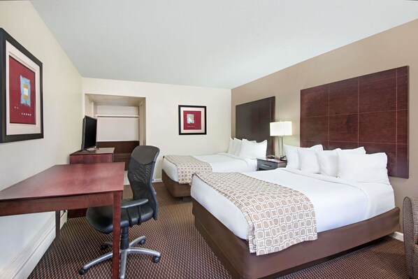 A hotel room with a desk, two beds, a chair, a TV, and framed pictures on the wall.
