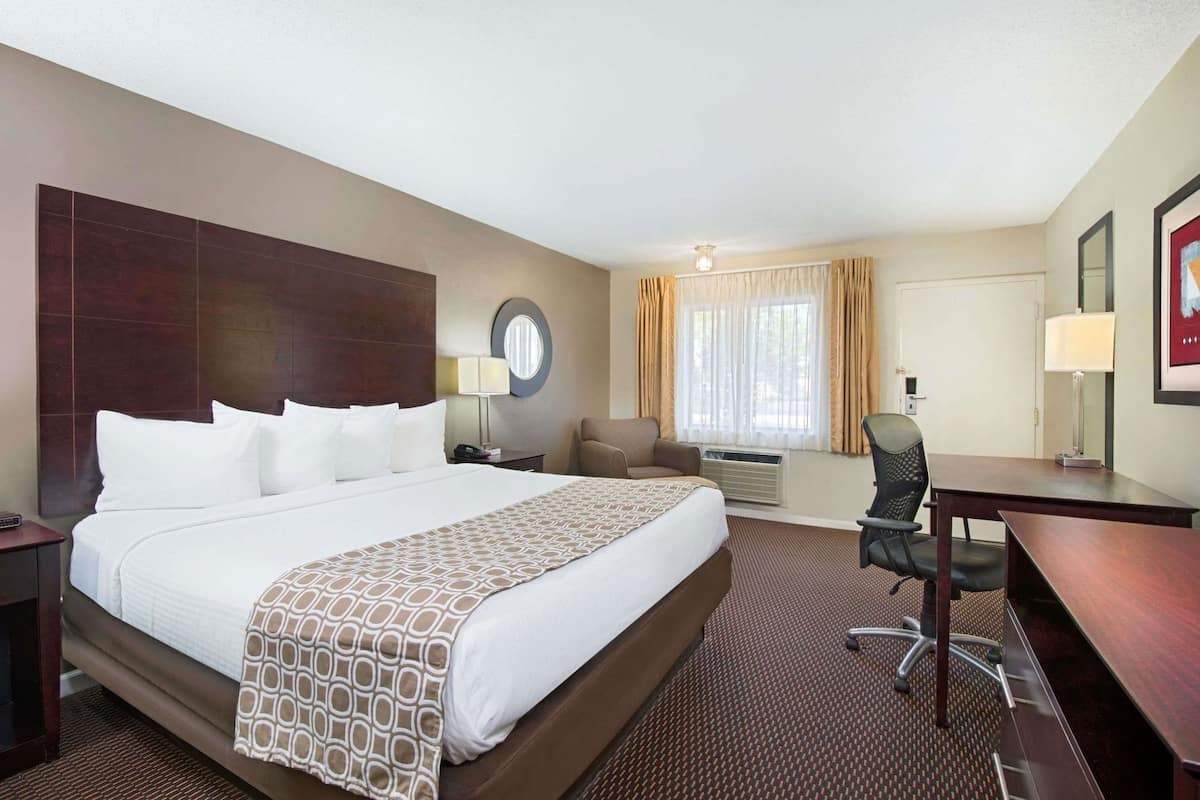 A hotel room with a large bed, a desk, a chair, a round mirror, and a window with curtains.