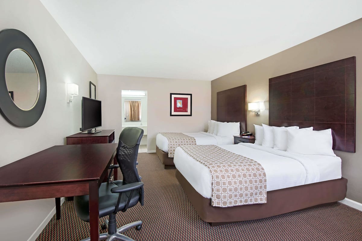 A hotel room with a desk, two beds, a chair, a TV, and a large mirror.