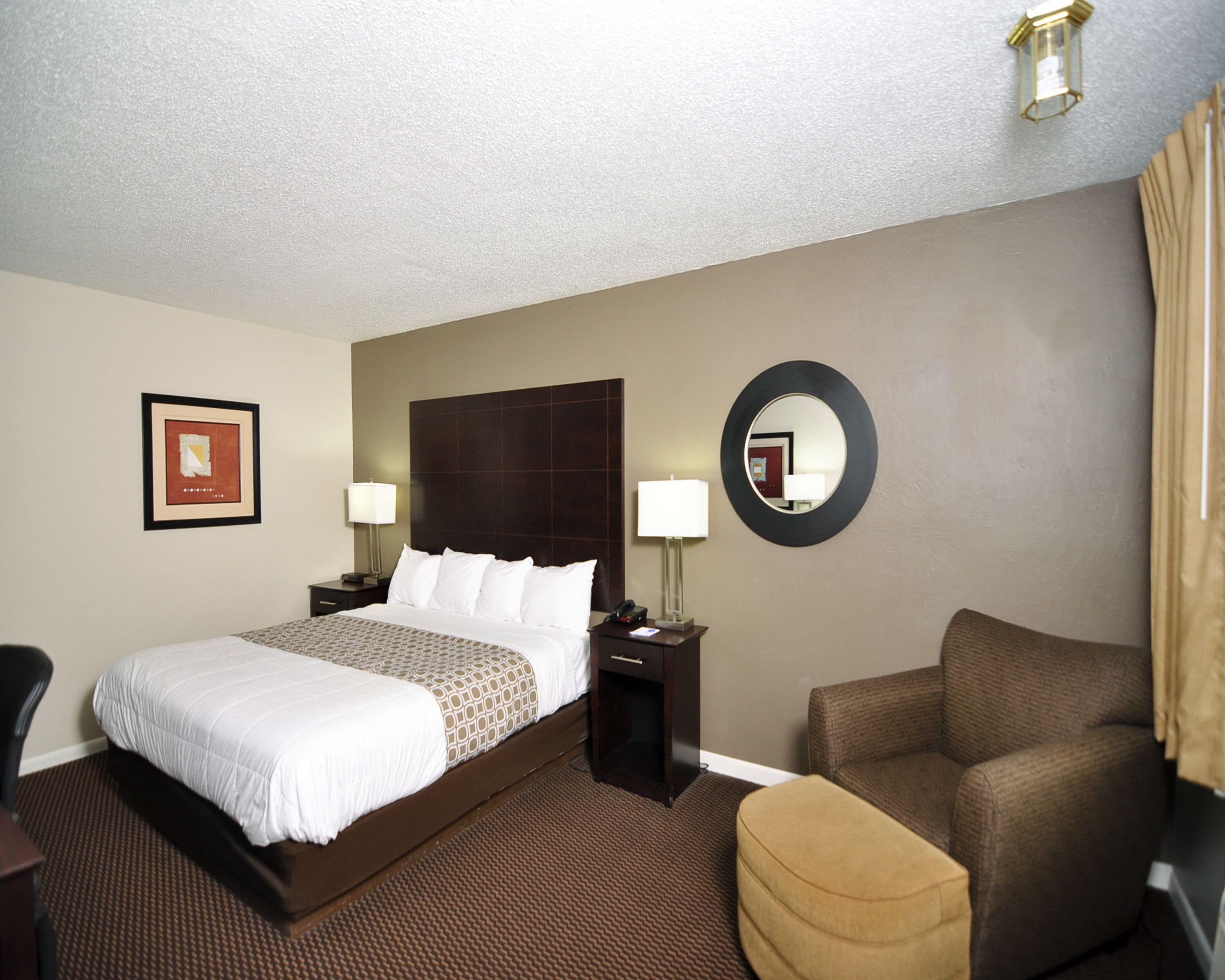 A hotel room with a large bed, a round mirror, a desk, and a chair.