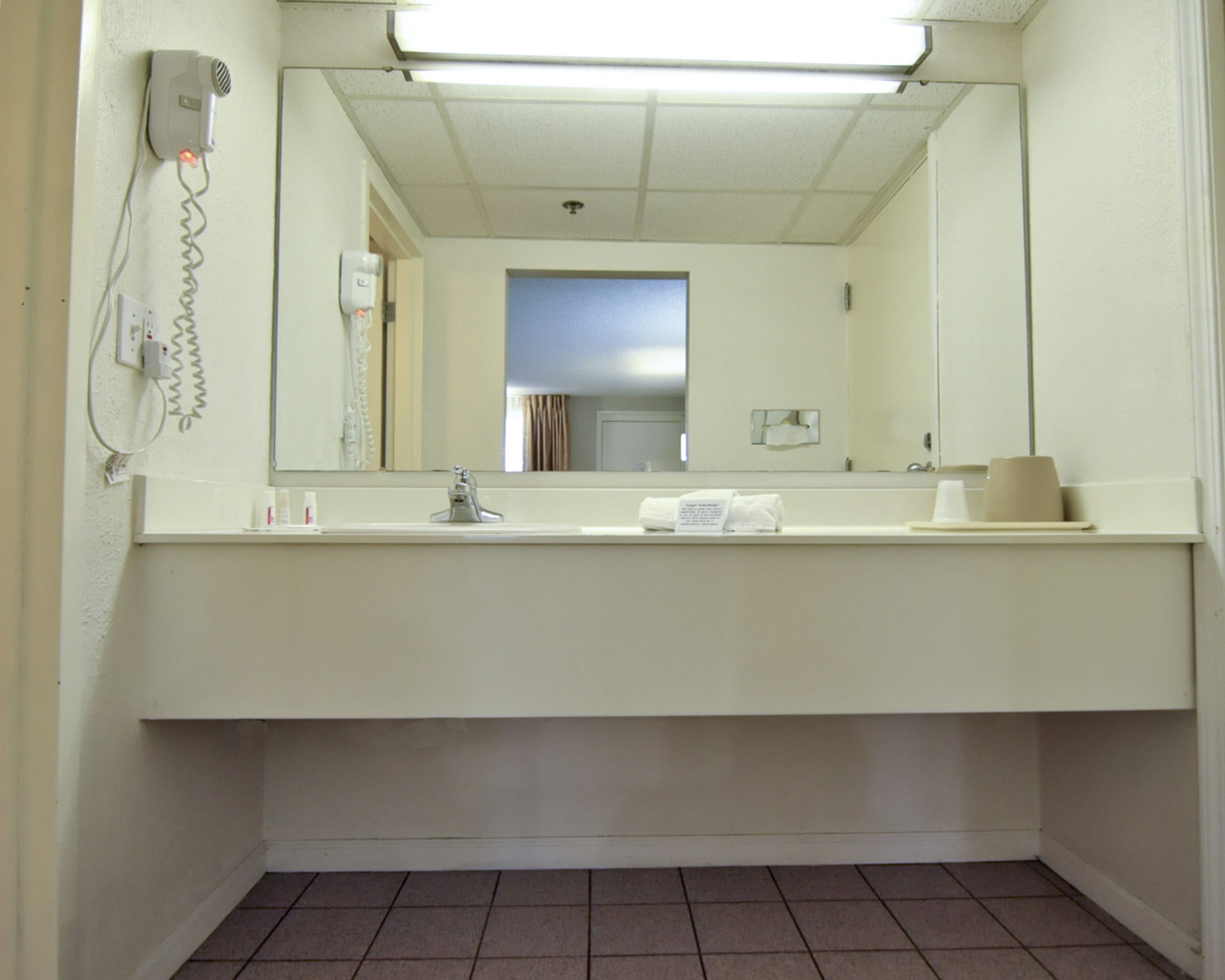 Une salle de bain d’hôtel avec un lavabo blanc, un miroir, un porte-serviettes et un sèche-cheveux fixé au mur.