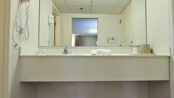 Une salle de bain d’hôtel avec un lavabo blanc, un miroir, un porte-serviettes et un sèche-cheveux fixé au mur.