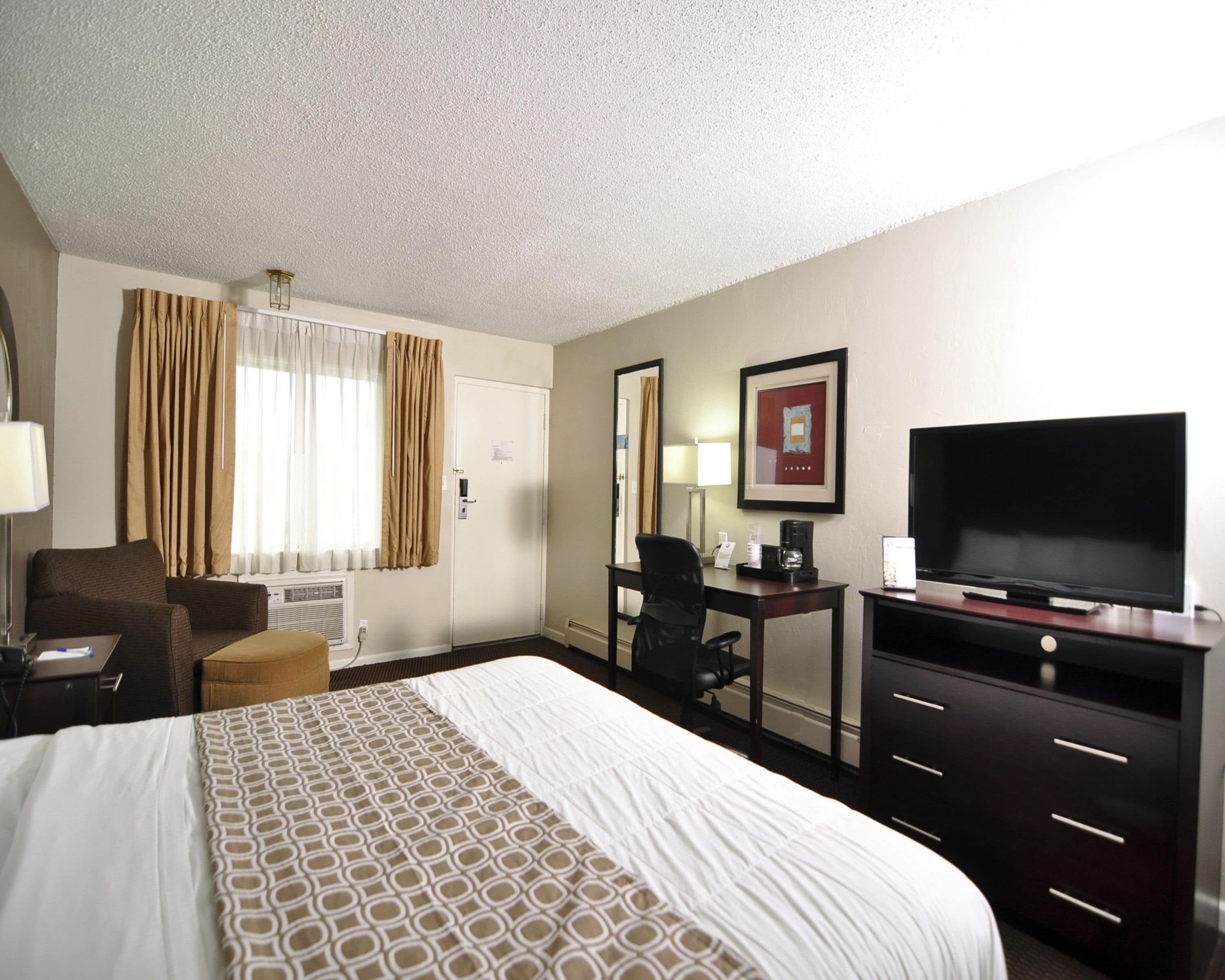 A hotel room with a large bed, a desk with a chair, a television, and a window with curtains.