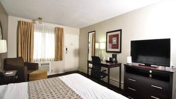 A hotel room with a large bed, a desk with a chair, a television, and a window with curtains.