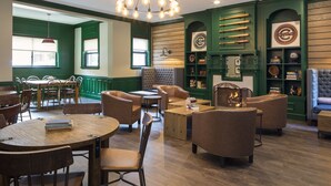Un espace salon accueillant avec des murs verts, des planchers en bois et des sièges en cuir. Des tables et des chaises y sont disposées pour permettre de prendre des repas et de socialiser.