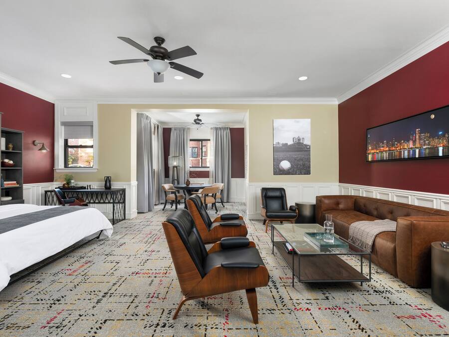 Habitación de hotel con una cama, una zona de estar con sillones de cuero, una mesa de centro, un televisor y un cuadro de paisaje urbano en la pared.