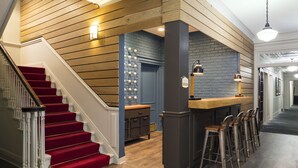 Un escalier recouvert d’une moquette rouge, des lambris en bois sur les murs et un coin bar avec des tabourets.