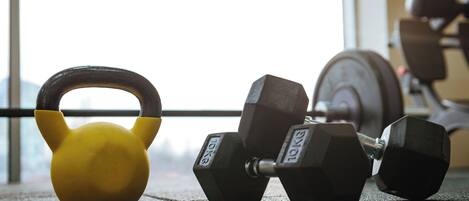 A yellow kettlebell and two black dumbbells on a gym floor with a window in the background.