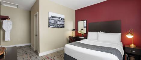 A hotel room with a large bed, a desk, a chair, a wardrobe, and a red accent wall.