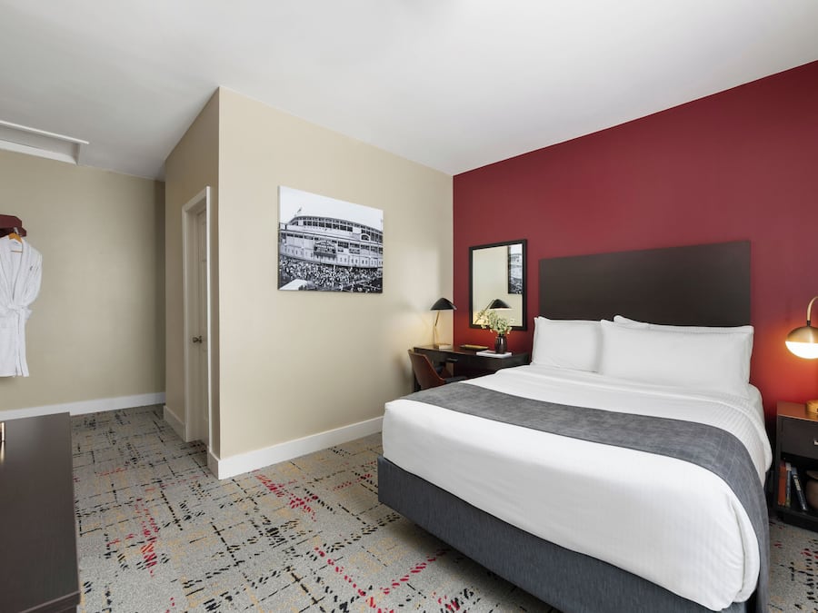 Quarto de hotel com uma cama grande, escrivaninha, cadeira, guarda-roupa e uma parede com detalhes em vermelho.