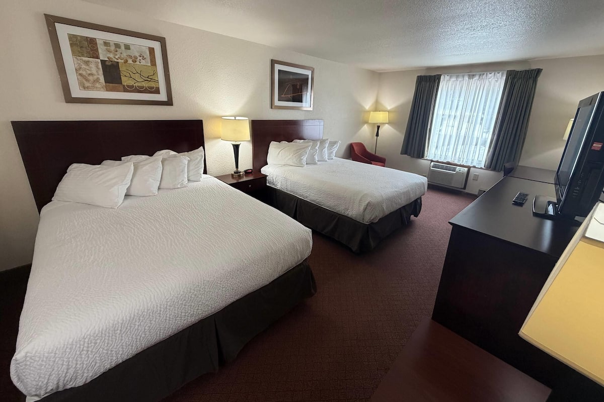 A hotel room with two beds, a desk, a TV, and a window with curtains.