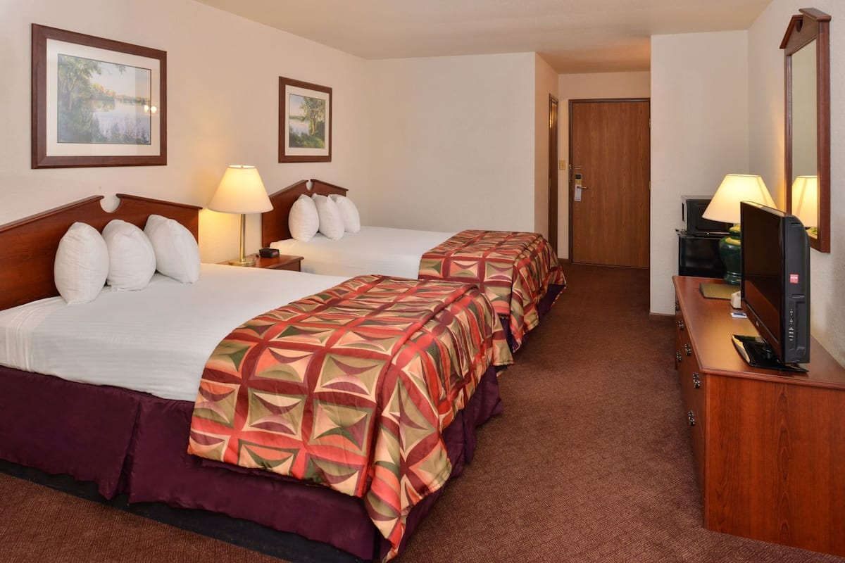A hotel room with two beds, a TV, and a door leading to another room.