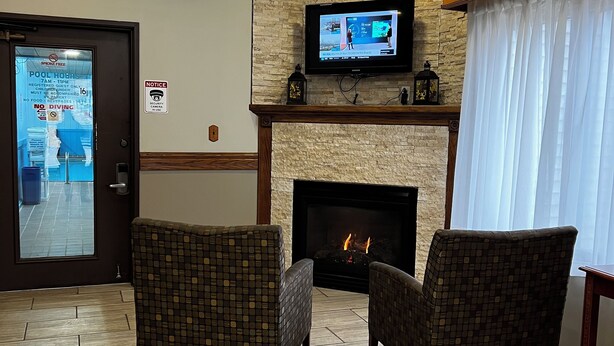 A lobby with two patterned armchairs, a fireplace, a television mounted on a stone wall, and a ceiling fan. - Travelodge by Wyndham Ishpeming/Marquette (Ishpeming)
