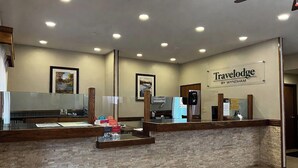 A reception desk with a sign reading 'Travelodge by Wyndham,' a framed picture on the wall, and a wooden counter. - Travelodge by Wyndham Ishpeming/Marquette (Ishpeming)