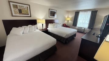 A hotel room with two beds, a desk with a television, a chair, and a window with curtains.