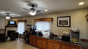 A spacious living area with a fireplace, a television, a coffee station, and a dining area with wooden cabinets and a herringbone-patterned floor. - Travelodge by Wyndham Ishpeming/Marquette (Ishpeming)