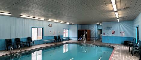 An indoor swimming pool with clear water, surrounded by tiled walls and a ceiling with fluorescent lights.