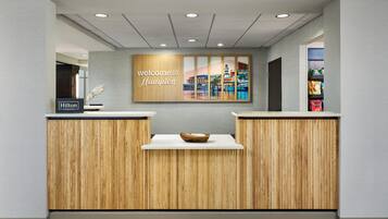 Una recepción con un cartel que dice 'Welcome to Hampton', un diseño de panel de madera y una obra de arte con vista a la ciudad.