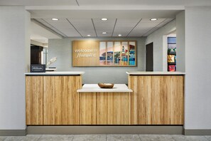 A reception desk with a 'Welcome to Hampton' sign, a wooden panel design, and a cityscape artwork above. - Hampton Inn & Suites Destin (Destin)