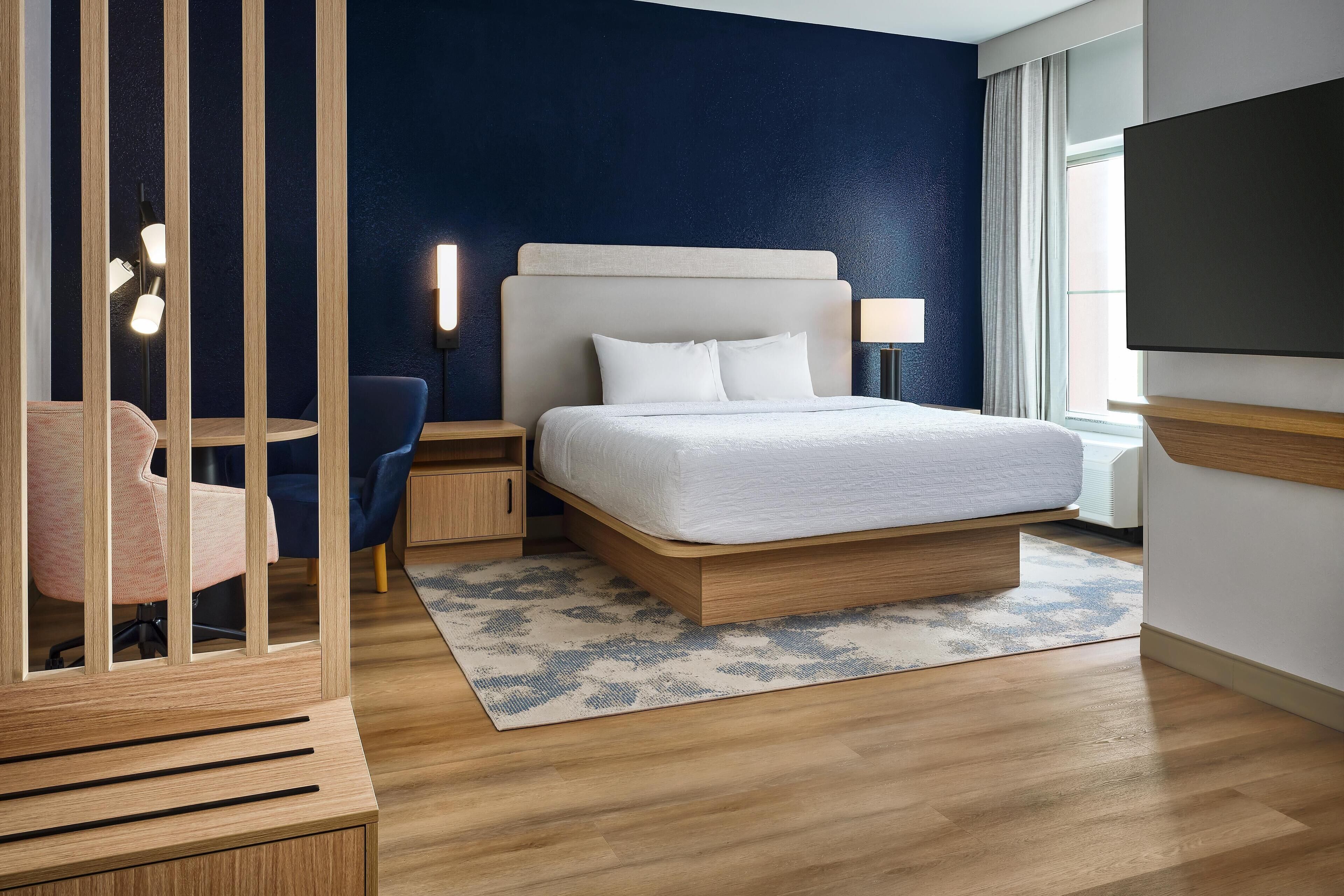 Una camera d'albergo moderna con un letto grande, una TV, una scrivania con una sedia e vista sull'esterno.