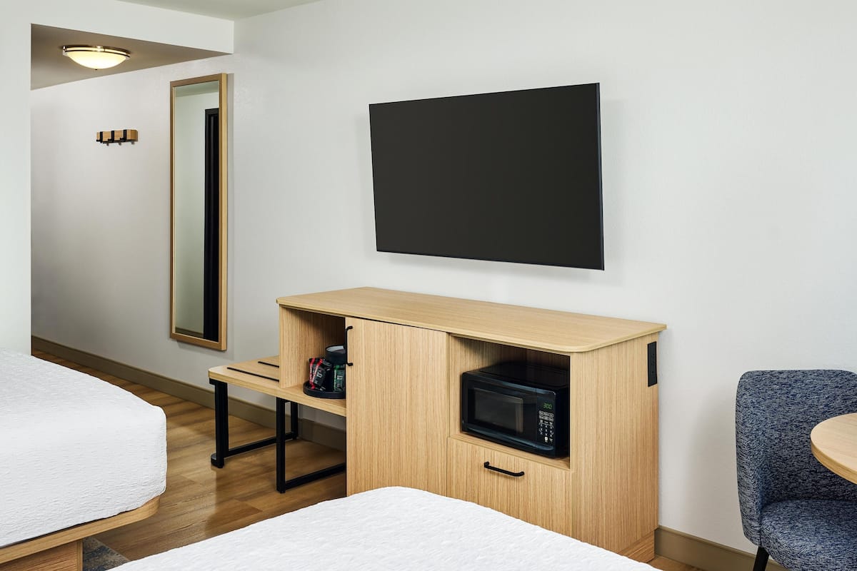 A hotel room with a bed, a desk with a microwave, a chair, and a large mirror.