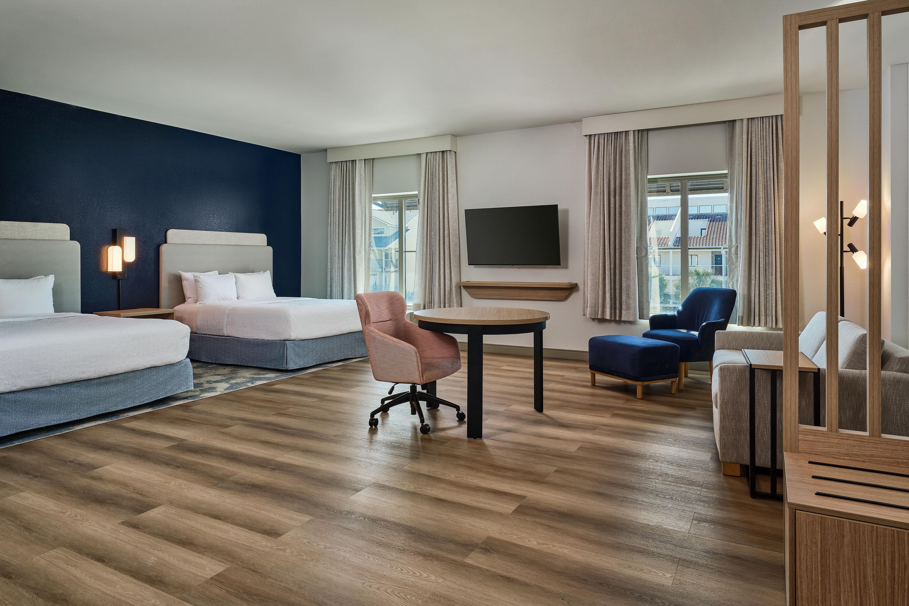 A hotel room with a bed, a desk, a chair, a TV, and a view of buildings through the window.