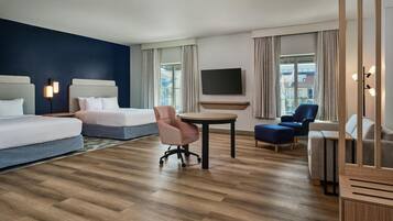 A hotel room with a bed, a desk, a chair, a TV, and a view of buildings through the window.