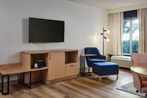 A modern living room with a flat-screen TV, a wooden cabinet, a blue chair, a red sofa, and a floor lamp. - Hampton Inn & Suites Destin (Destin)