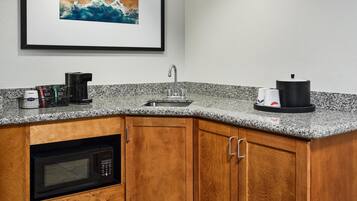 A kitchen with a granite countertop, a coffee maker, a kettle, and a microwave.