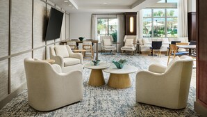Un moderno vestíbulo de hotel con una televisión grande, asientos cómodos, una mesa de centro y vistas al exterior.