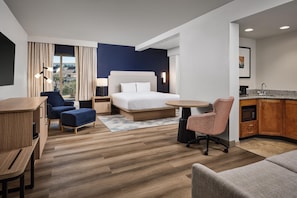 A hotel room with a bed, a desk, a chair, a kitchenette, and a view of the outside. - Hampton Inn & Suites Destin (Destin)