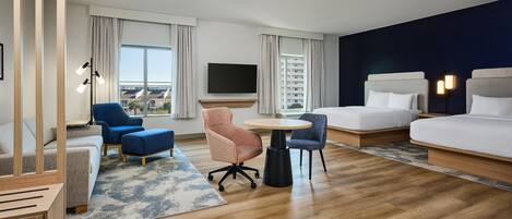 A hotel room with a bed, a desk, two chairs, a TV, and a view of a building.