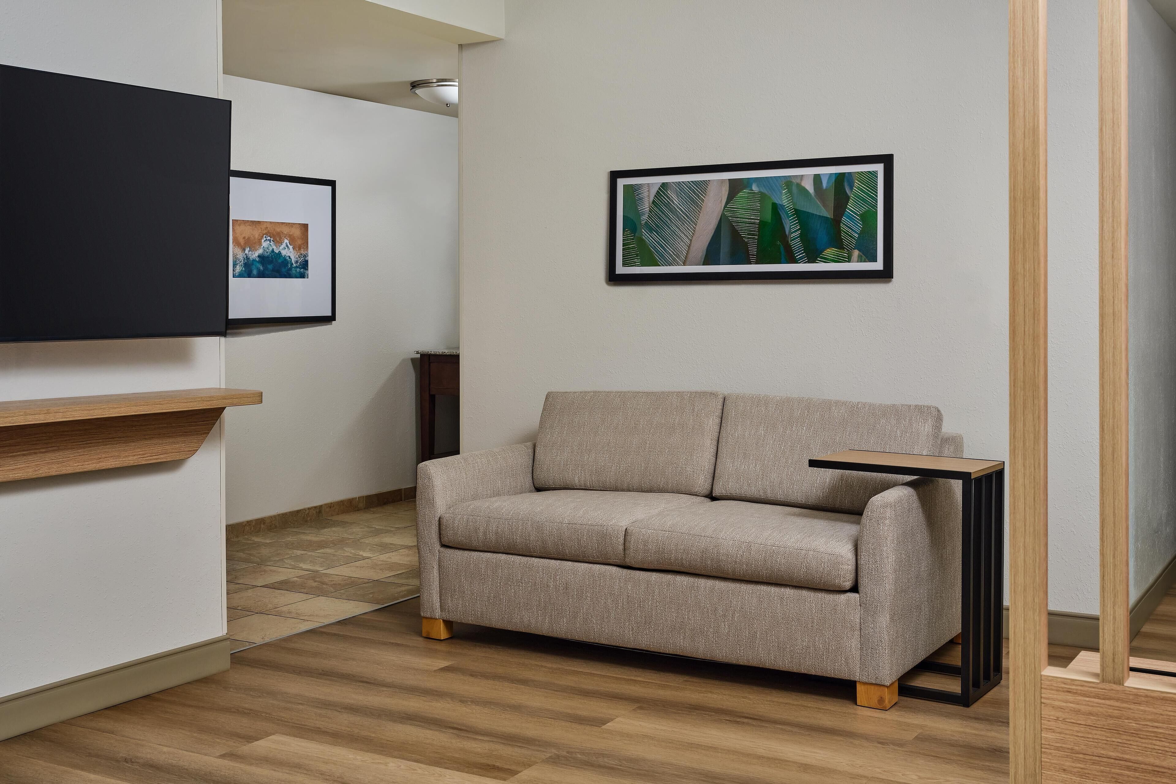 A modern living room with a beige sofa, a small wooden side table, and two framed artworks on the wall.