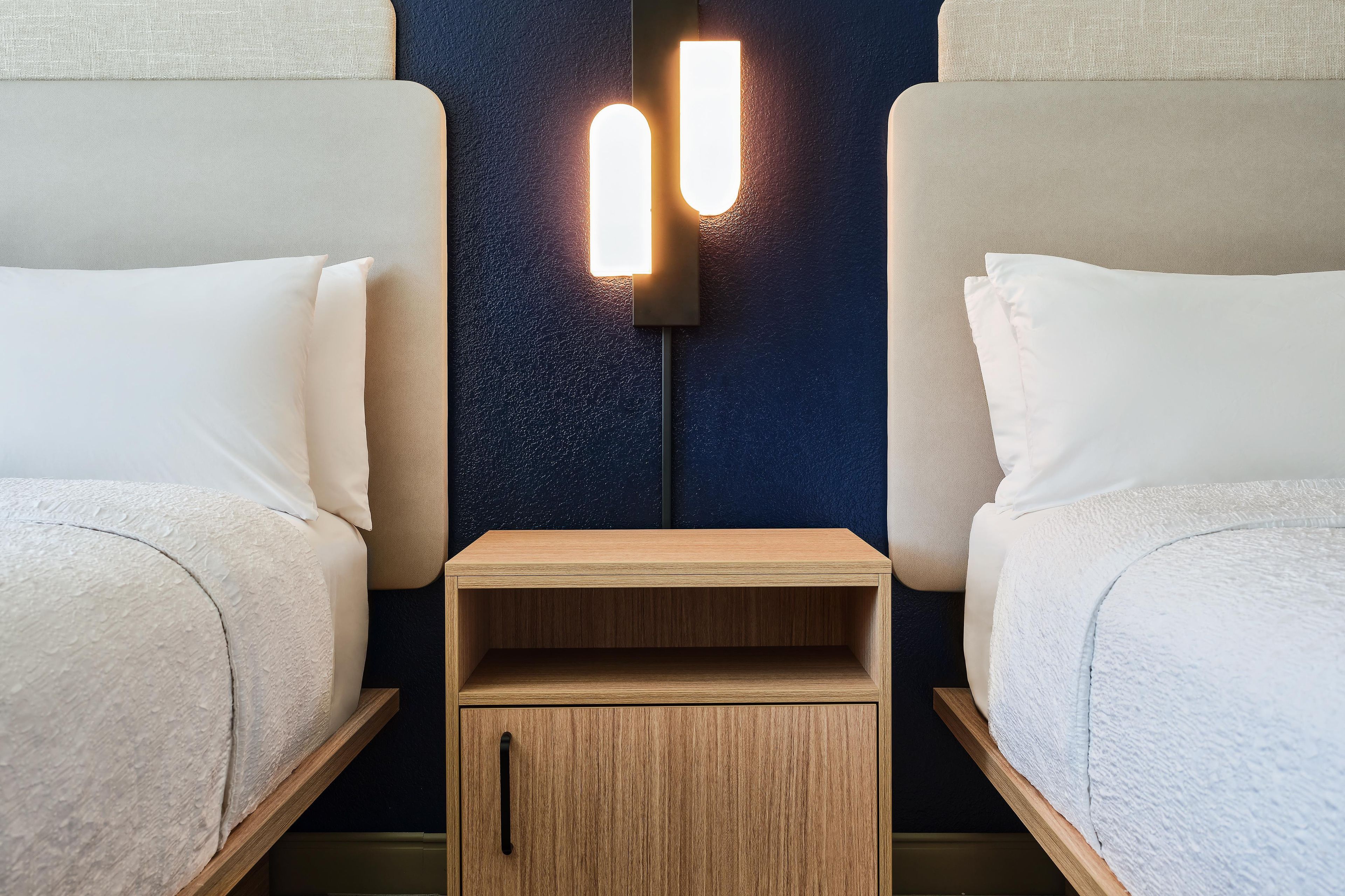 Une chambre d’hôtel avec deux lits, une table de chevet et un luminaire fixé au mur.