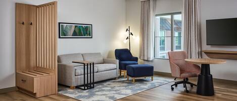 A modern living room with a sofa, two armchairs, a coffee table, a TV, and a large window with curtains.