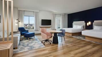 Une chambre d’hôtel équipée d’un lit, d’un bureau, de deux chaises, d’une télévision et offrant une vue sur les bâtiments.