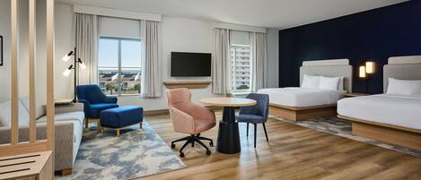 Habitación de hotel con cama, escritorio, dos sillas, televisor y vista a edificios.