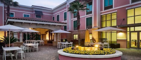 A courtyard with outdoor seating, a central water feature, and a building with large windows.