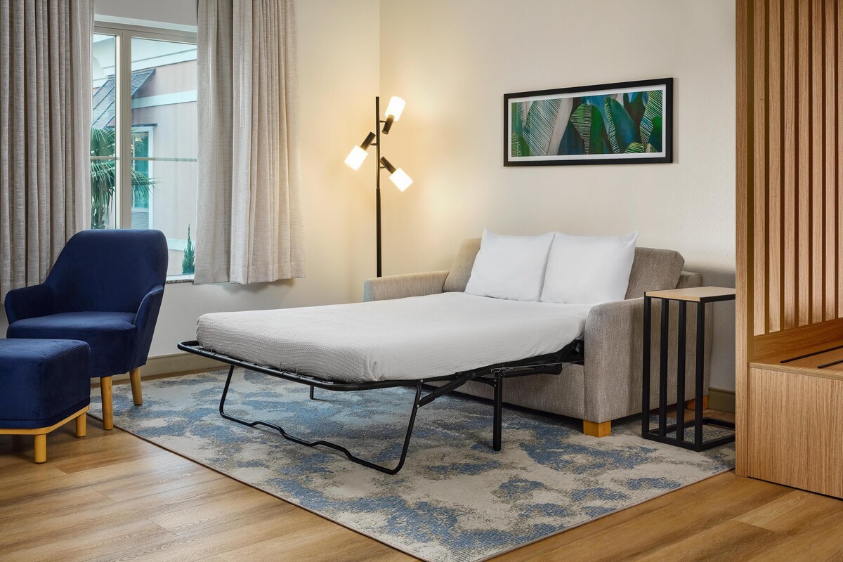 A modern bedroom with a bed, a blue chair, a small table, and a floor lamp.